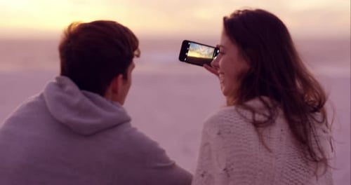 4k video footage of a couple using a smartphone to take selfies on the beach at sunset