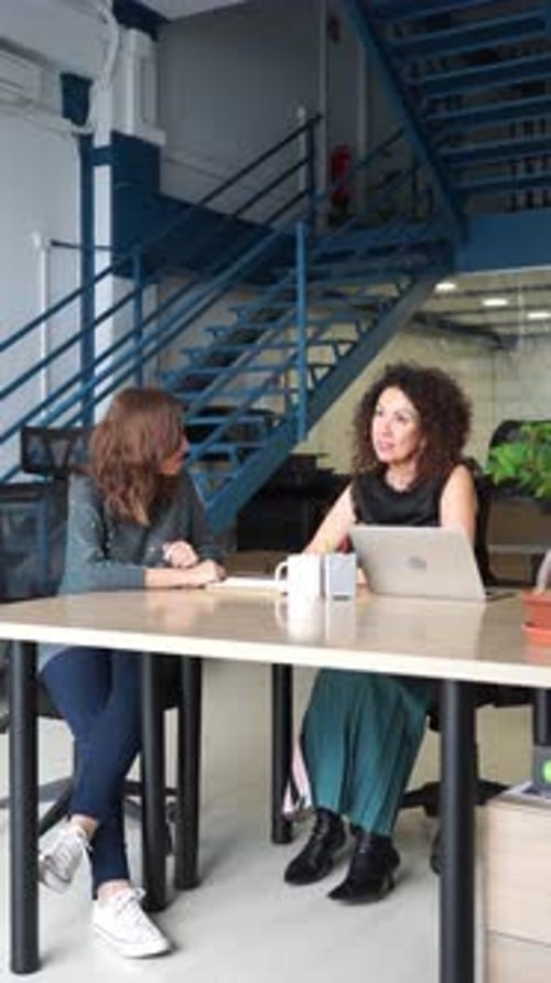 Two women talk across a desk in modern office