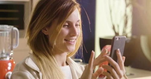 Smiling Woman Using Smartphone in Modern Kitchen