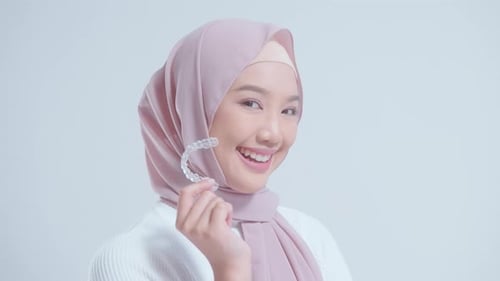 Young smiling muslim woman with hijab holding invisalign braces in studio