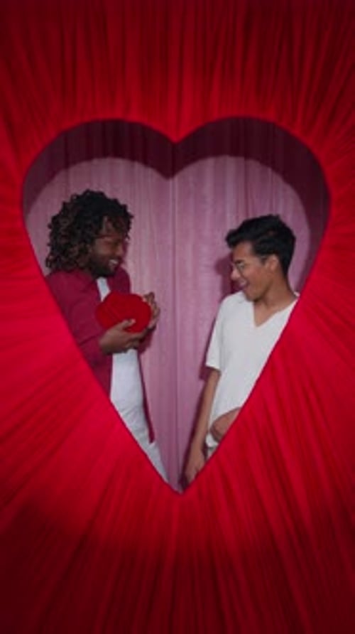 Male Couple Sharing Chocolates in Heart Valentine Booth