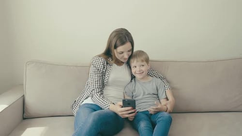 Smiling Mother and Child Using Phone on Couch