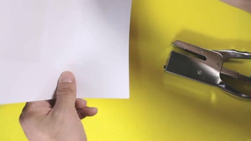 A silver metallic stapler fastens a collection of printed papers, forming an angled crimped junction