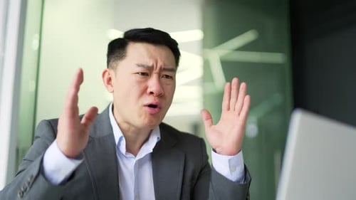 Close up. Angry asian man in formal suit arguing talking on video call on laptop while sitting