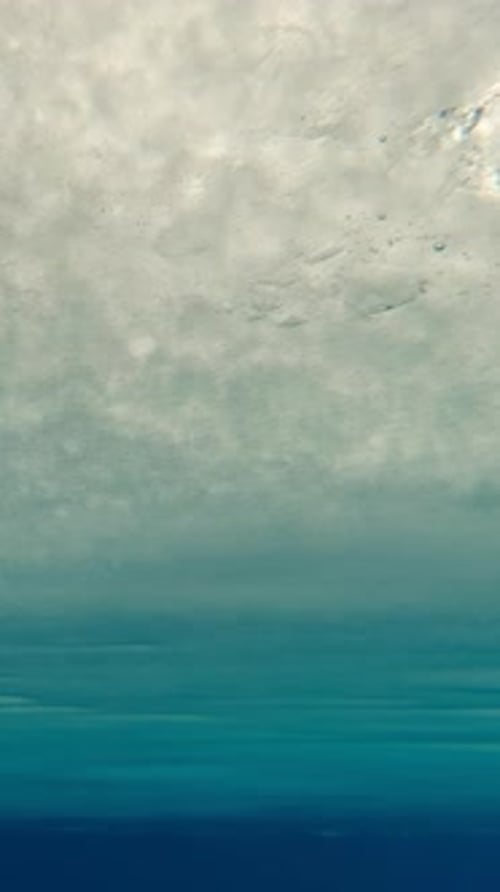 Vertical footage, movement under solid layer of ice in blue water in evening light