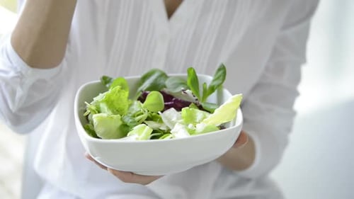 Close Up Shot Of A Woman Holding A Plate Of Fresh Green Salad In The Beautiful Morning Light. She...