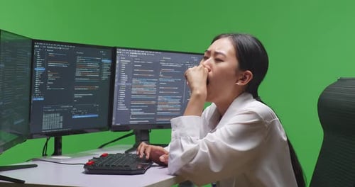 Tired Asian Woman Developer Yawning While Write Code With Multiple Screens In Green Screen Studio