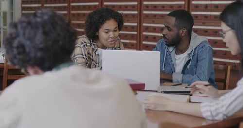 Diverse Group of Students Doing Research in Library Using Laptop Talking and Reading Books