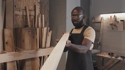 Adult Inspects Wood Plank in Workshop