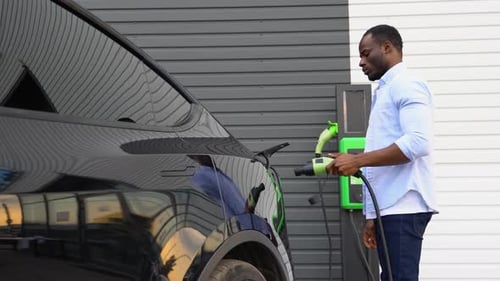 African American Man Disconnects Power Connector Into Luxury EV Car at Station
