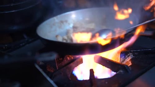 Stirring Meat Pieces In Pan On Gas Stove With Bright Orange Flames