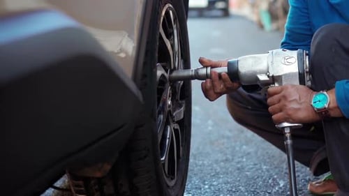 Man Changes Car Tire with Pneumatic Wrench on Street