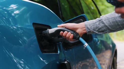 Close up Man plugging an electric car or EV at charging station at green. Save ecology alternative e