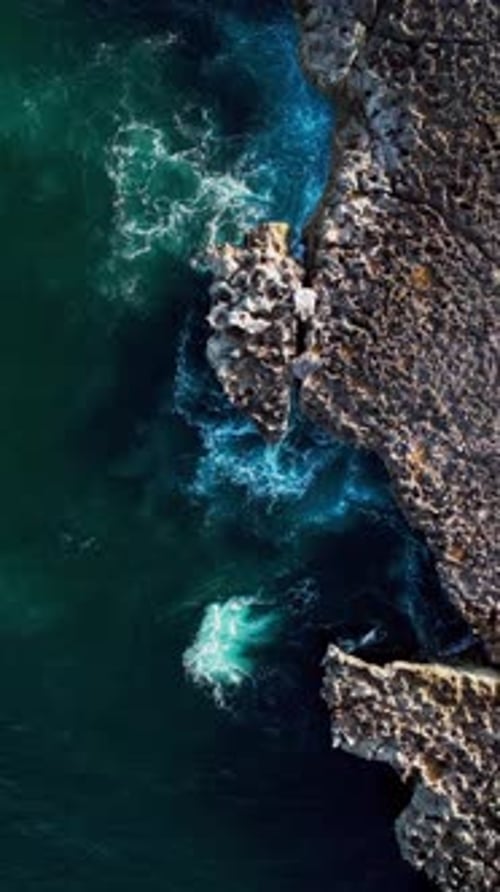 Overhead Vertical aerial of jagged lava shoreline with ocean water and rugged natural coastal rocks