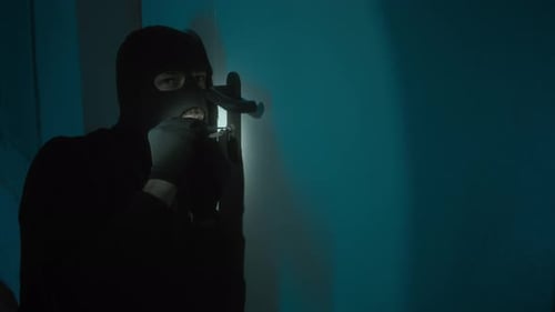 Junger männlicher Krimineller in Sturmhaube versucht mit Lockpick die Tür zu öffnen