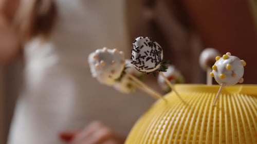 The confectioner dips a strawberry on a skewer into pink chocolate, while a ready strawberry