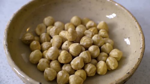 Un jet de noisettes pelées dans un petit bol beige qui tourne lentement.