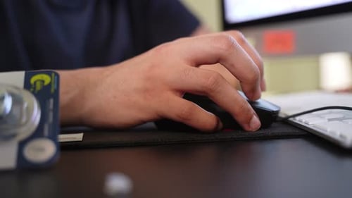 Hand Using Computer Mouse at Office Desk Beside Keyboard and Monitor