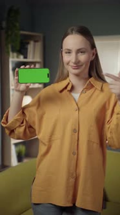 Young Woman Smiling and Holding a Modern Smartphone Horizontally with a Blank Green Screen for App