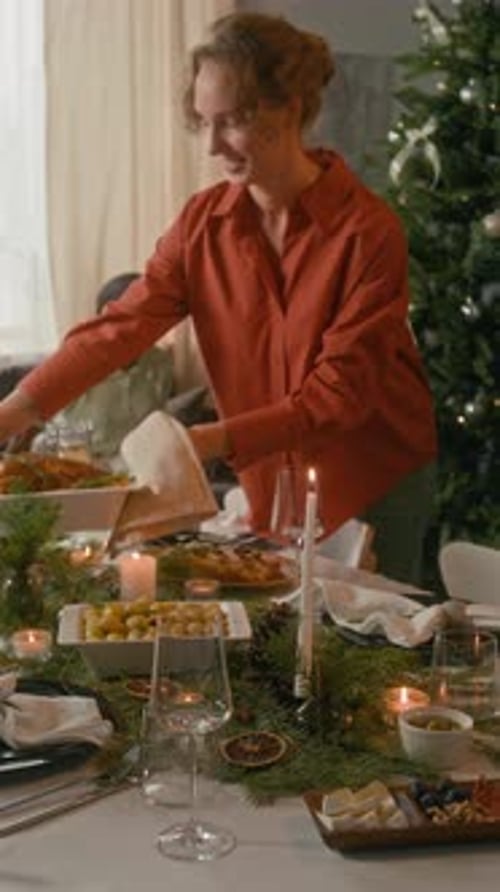 Young Woman Bringing out Roasted Chicken, Friends Taking Places at Holiday Table