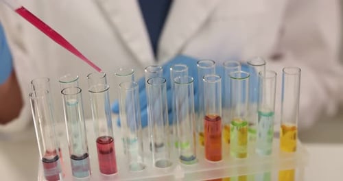 Scientist dripping reagent into test tubes in laboratory, camera moving right. Solution chemistry