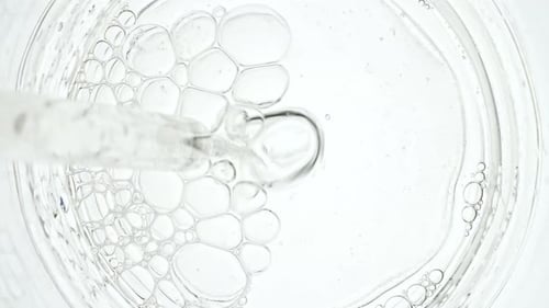 Des bulles d'air transparentes sortent d'une pipette de laboratoire et éclatent à la surface d'un liquide clair à Petri