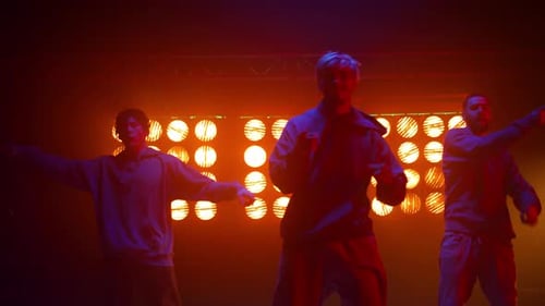 Three young men dancing on stage with bright lights