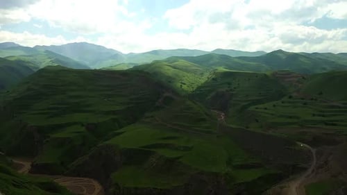 Green Hillside with a Small Town in the Distance and Mountains in the Distance with a Few Clouds