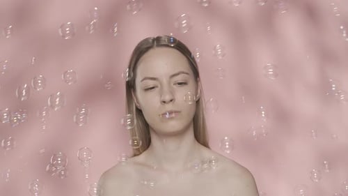 A Woman with Naked Shoulders in the Studio Surrounded By Soap Bubbles on a Pink Background A Woman