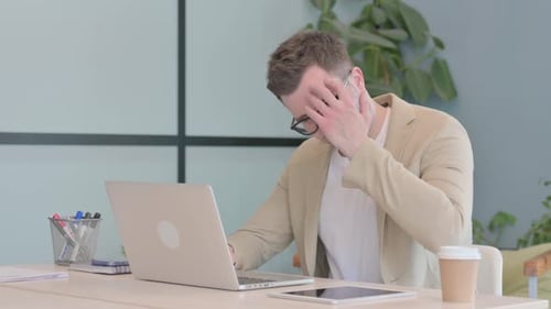 Young Adult Man Working on Laptop Rubbing Forehead