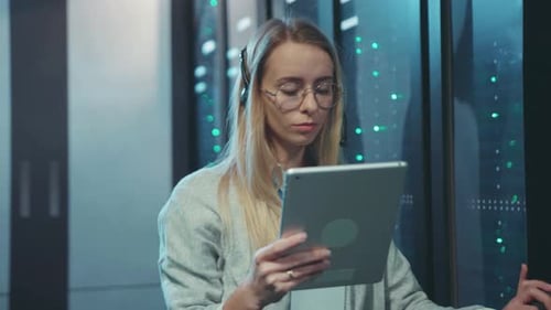 A Skilled Female Technician is Diligently Working in a Data Center Utilizing a Tablet