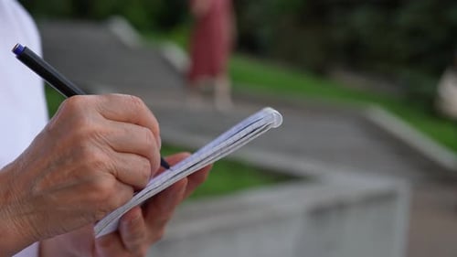 Adult Writes in Notebook in Urban Park