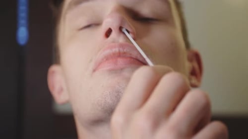 Man Rotating Sterile Nasal Swab Around Its Nostril, COVID-19 Test Kit At Home. - close up
