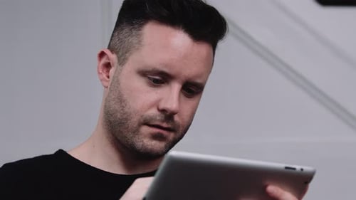 Man Looks at Tablet Screen in Bright Indoor Setting