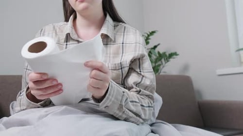 Femme malade enveloppée dans une couverture tenant des mouchoirs, utilisant des serviettes en papier pour le nettoyage nasal en cas de froid