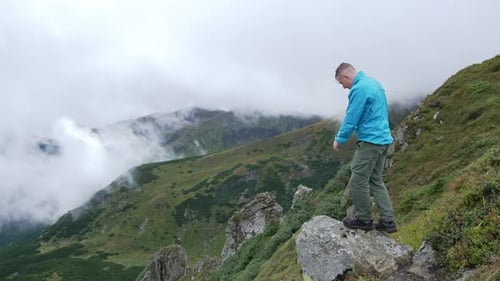 A man is standing on top of a mountain and rejoices, jumps, hands up