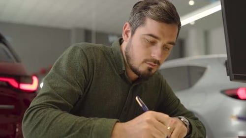 man completes a form in a car dealership showroom