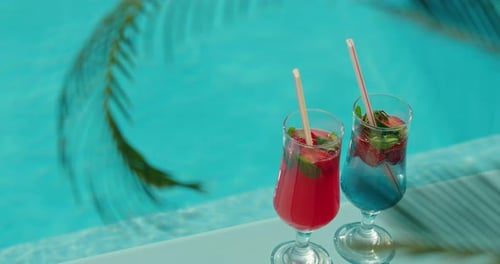 Zwei farbenfrohe Sommercocktails mit frischen Erdbeeren und Minze am Rand eines Schwimmbades