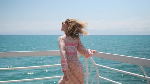 Rear view, attractive young girl dancing with the sea wind blowing her hair, expressing joy