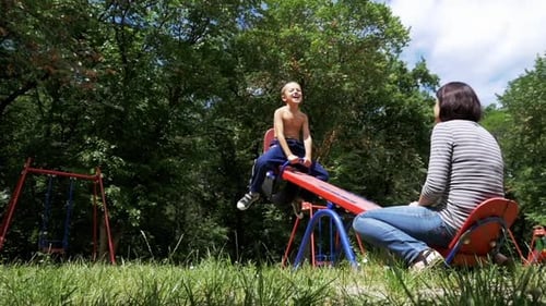 Happy Child Boy and His Mother Swinging on a Street Counterweight Swing at Playground in Slow Motion