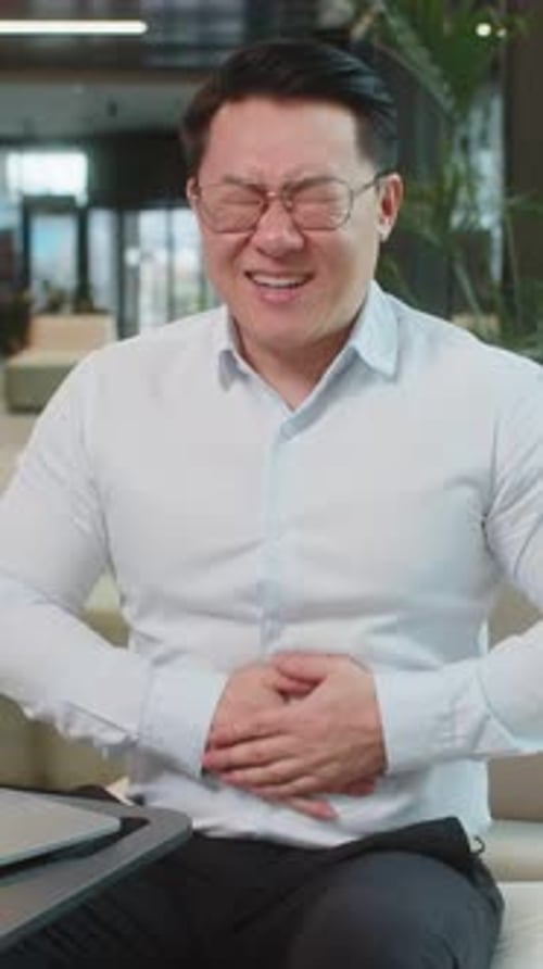 Disappointed Chinese Businessman Using Laptop and Feeling Sudden Stomach Ache in Office Lobby