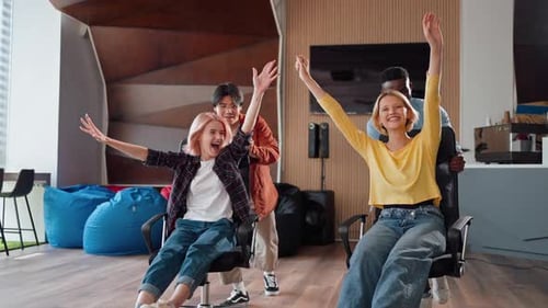 Wide Shot Young Pretty Women Sitting on Office Chairs and Their Colleagues Rolling Them Along Office