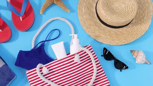 Tasche mit verschiedenen Strandaccessoires auf hellblauem Hintergrund, flach liegend