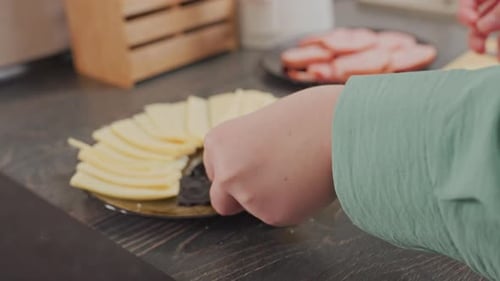Femme arrangeant du fromage tranché sur une assiette noire à partir d'une planche à découper en bois