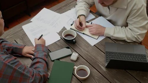 Gen Z Specialists Discussing Papers and Taking Notes in Outdoor Cafe