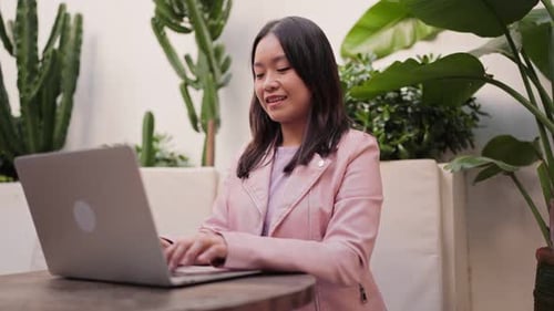 Focused Asian Woman Using Laptop at Outdoor Cafe