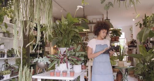 Woman Using Tablet Amongst Indoor Plants in Shop