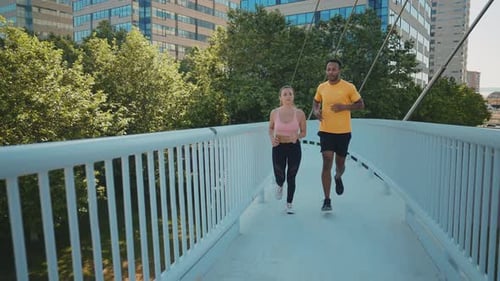 Athletic Man and Woman Jogging Across Urban Bridge