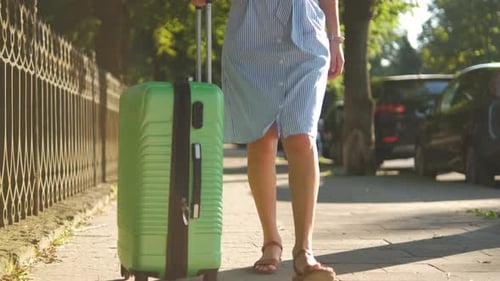 Gros plan d'une jeune femme marchant sur le trottoir de la ville avec une valise verte un jour d'été
