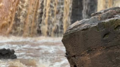 Muddy river water flows over stone dam in background after storm